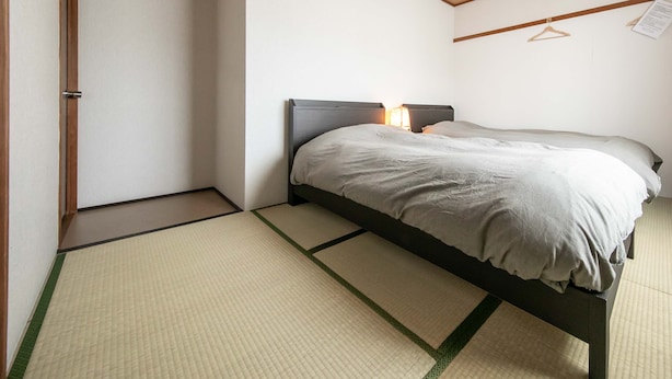 A room with a bed, a hanging light fixture, and a wooden ceiling. - Guest House MEETS Okayama (Okayama)