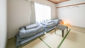 A room with a futon bed, a small table, a hanging light, and a wooden ceiling. - Guest House MEETS Okayama (Okayama)