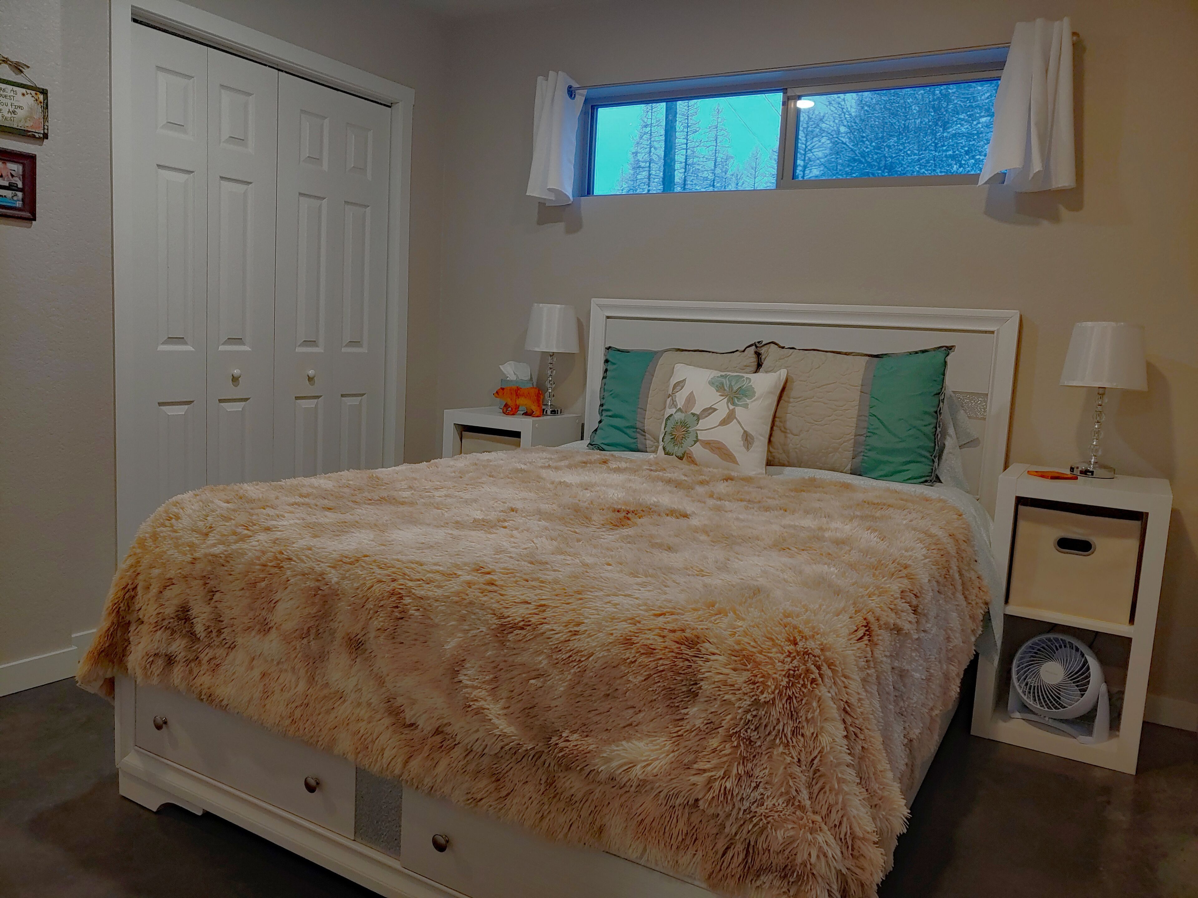 A bedroom with a bed, two bedside tables, a window with curtains, and a door.