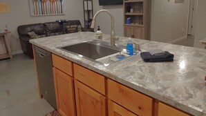 Une cuisine moderne dotée d’un grand îlot central, d’un évier en acier inoxydable, de meubles de rangement en bois et d’un téléviseur à écran plat fixé au mur.