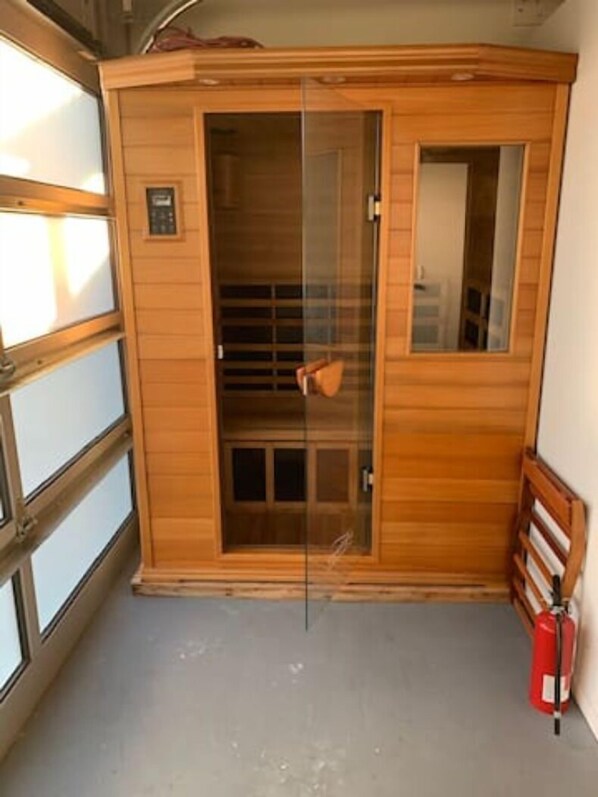 A sauna room with a glass door, wooden walls, and a fire extinguisher on the floor. - Ocean View House Few Steps from Miramar Beach (Half Moon Bay)
