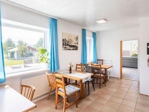 Ein Essbereich mit Tisch und Stühlen, einem Heizkörper, einem Fenster mit Vorhängen und einem Bild an der Wand.