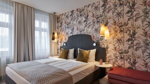 Hotellihuone, jossa on suuri sänky, kaksi yöpöytää, punainen penkki ja kukallinen tapetti.