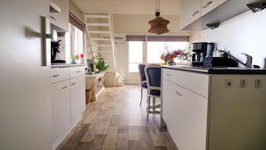 A modern kitchen with white cabinets, a wooden floor, a built-in ladder, a coffee maker, and a chair. - Nice apartment in Bruinisse (Bruinisse)
