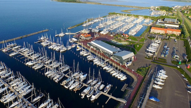 An aerial view of a marina with numerous boats docked, a large building with a red roof, and a parking area with cars. - Nice apartment in Bruinisse (Bruinisse)