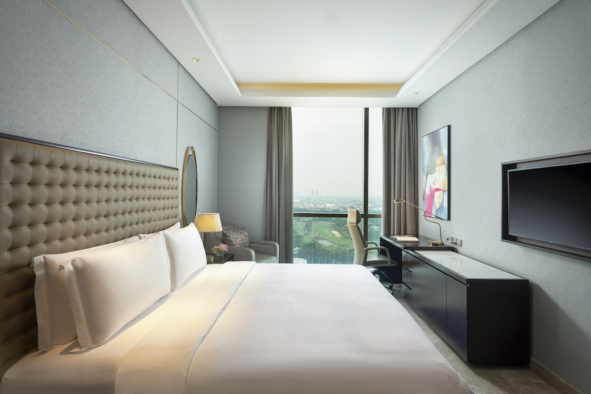 A modern hotel room with a large bed, a desk, and a TV.