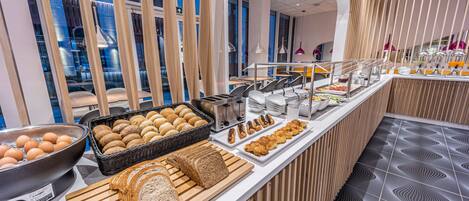 A buffet with various food items, including bread, pastries, and a bowl of eggs.