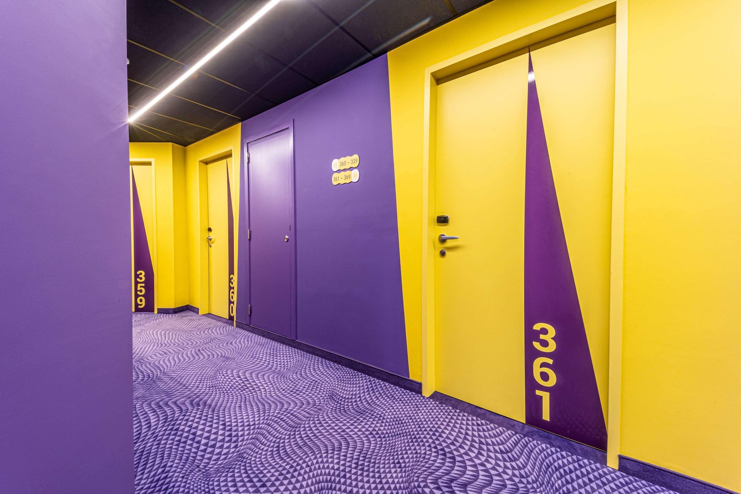 A hotel hallway with purple and yellow walls, numbered doors, and a patterned floor.