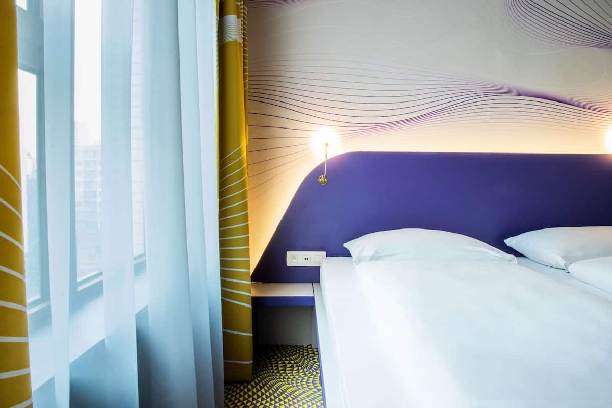 Ein Hotelzimmer mit Bett, Nachttisch und einem Fenster mit Vorhängen.
