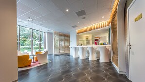 A modern lobby with a reception desk, seating area, and large windows offering a view of greenery. - Prize by Radisson, Antwerp City (Antwerp)