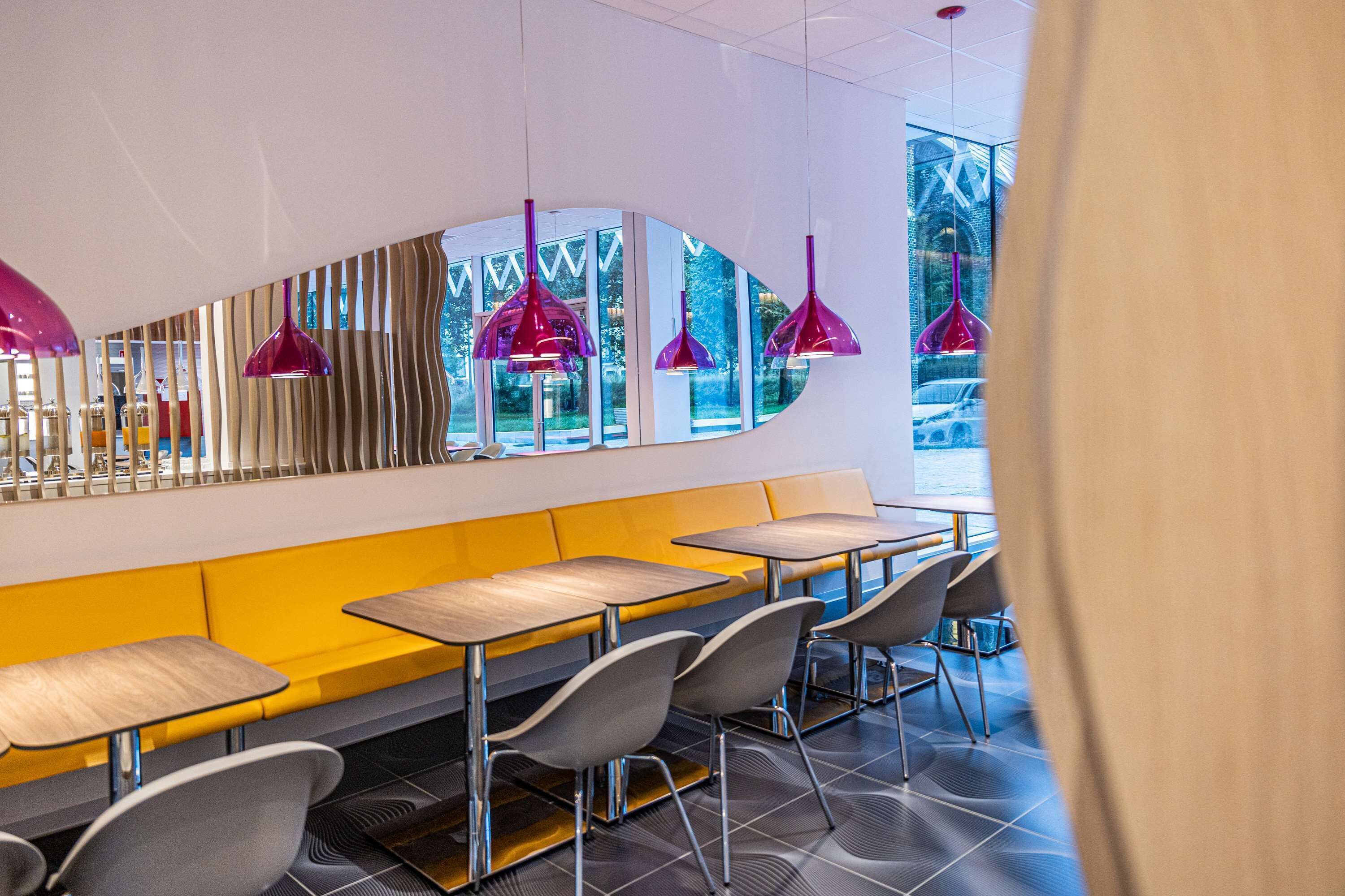 A modern restaurant with yellow booths, grey chairs, and purple pendant lights.