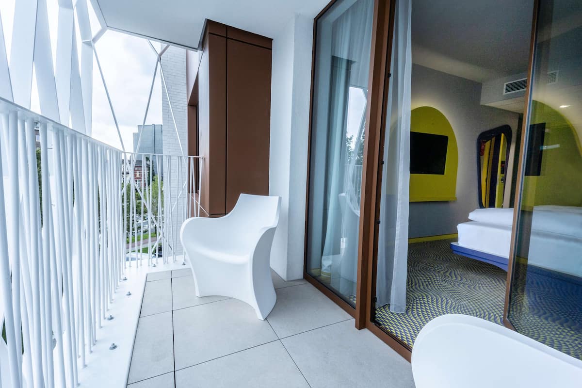 Ein modernes Hotelzimmer mit Balkon, einem weißen Stuhl und einem Bett mit gemustertem Teppich.