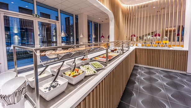 A buffet area with various food stations, a glass railing, and a modern interior design. - Prize by Radisson, Antwerp City (Antwerp)