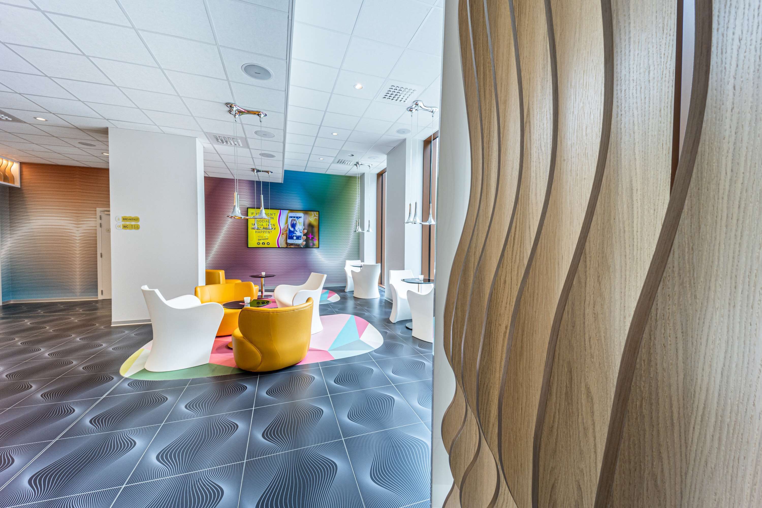 Un interno moderno con pavimento decorato, un'area reception con televisore e posti a sedere colorati.