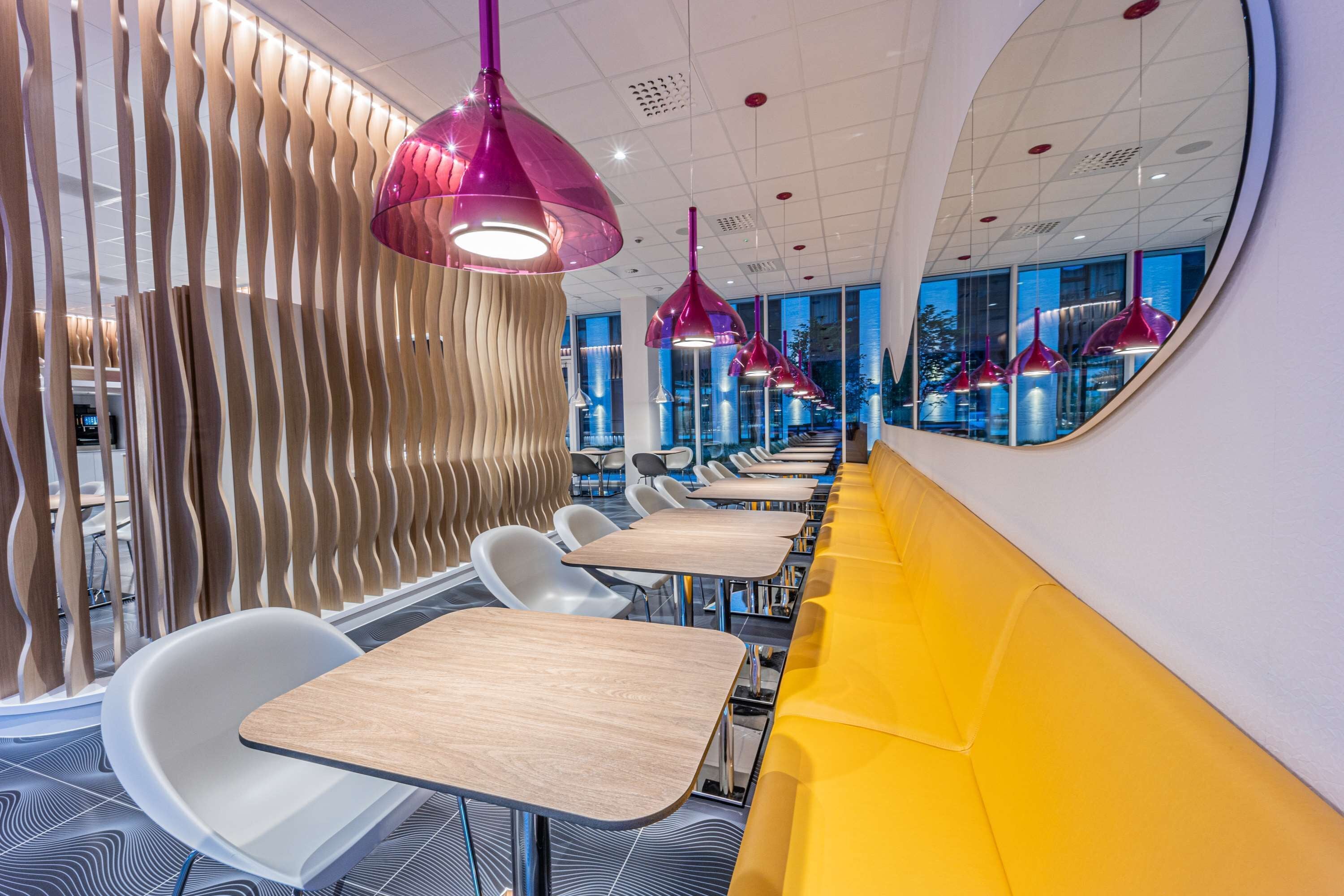 Interior modern d'un restaurant amb una barra llarga, cadires blanques i seients de color groc vibrant.