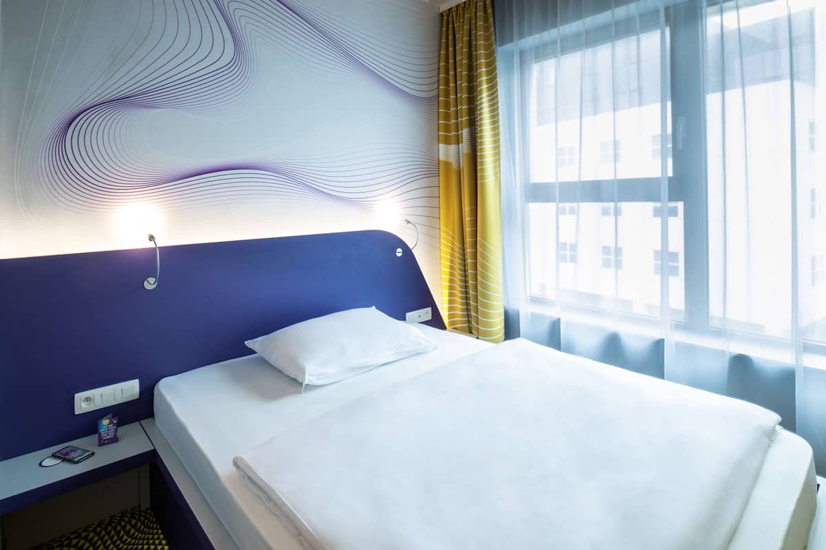 Ein Hotelzimmer mit blauem Kopfteil, einem weißen Bett, einem Nachttisch mit Telefon und einer Wand mit wellenartigem Muster.