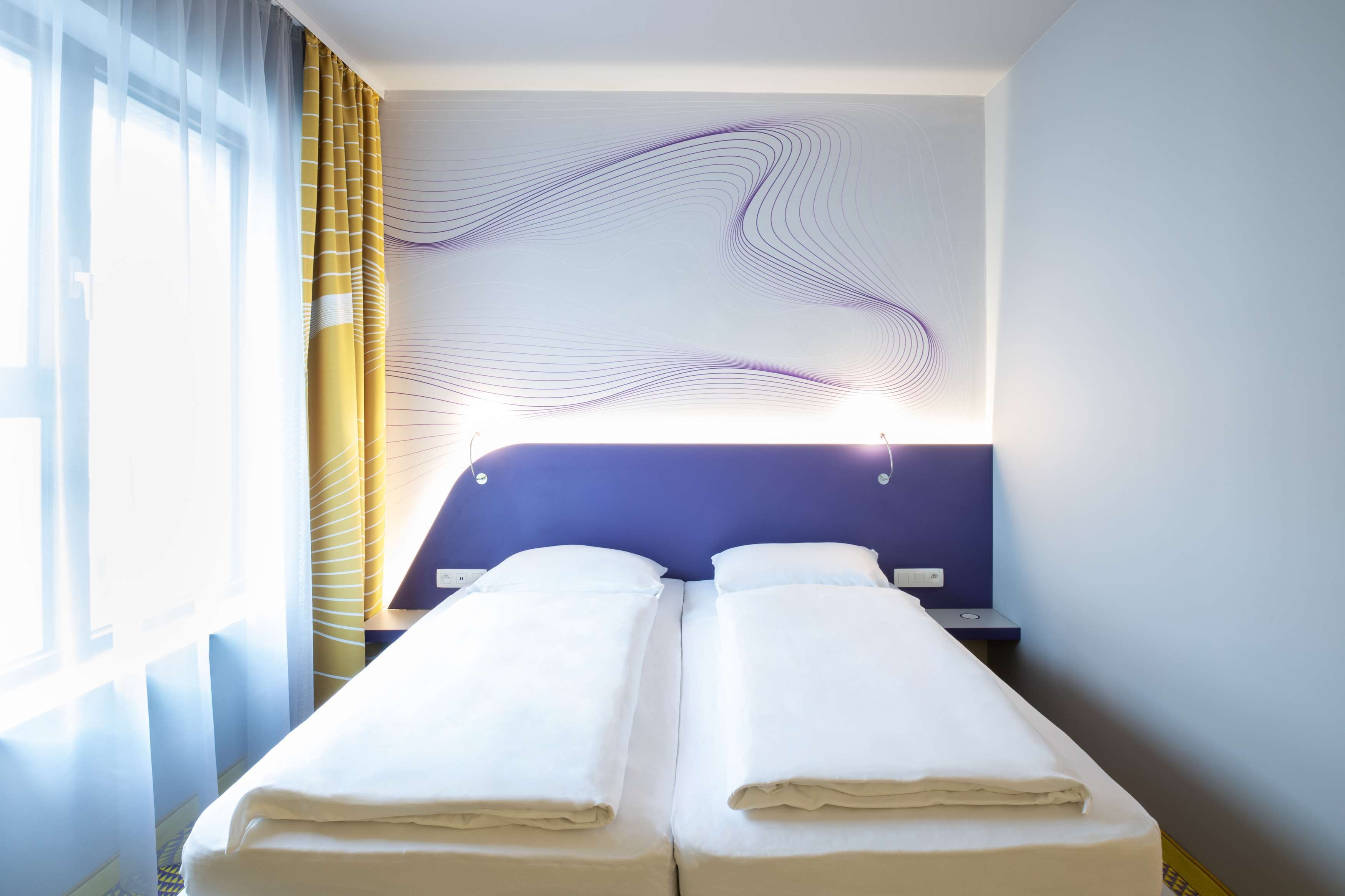 Quarto de hotel com cama, cortinas e uma parede com padrão ondulado.