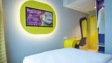 A modern hotel room with a bed, a desk, and a TV displaying a welcome message.