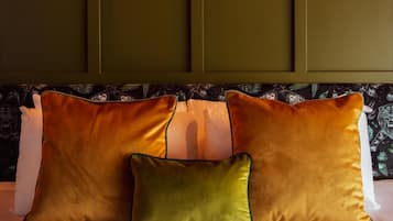 Una cama con tres almohadas en tonos naranja y verde, un cabecero estampado y una pared lisa detrás.