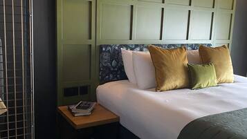 A hotel room with a large bed, a small bedside table, a nightstand, and a wall-mounted light fixture.