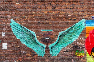 Un muro de ladrillo con un gran mural turquesa de un ángel y un logotipo colorido.