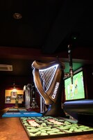 A bar area with a Guinness branded harp, a television displaying a sports game, and a selection of bottles.