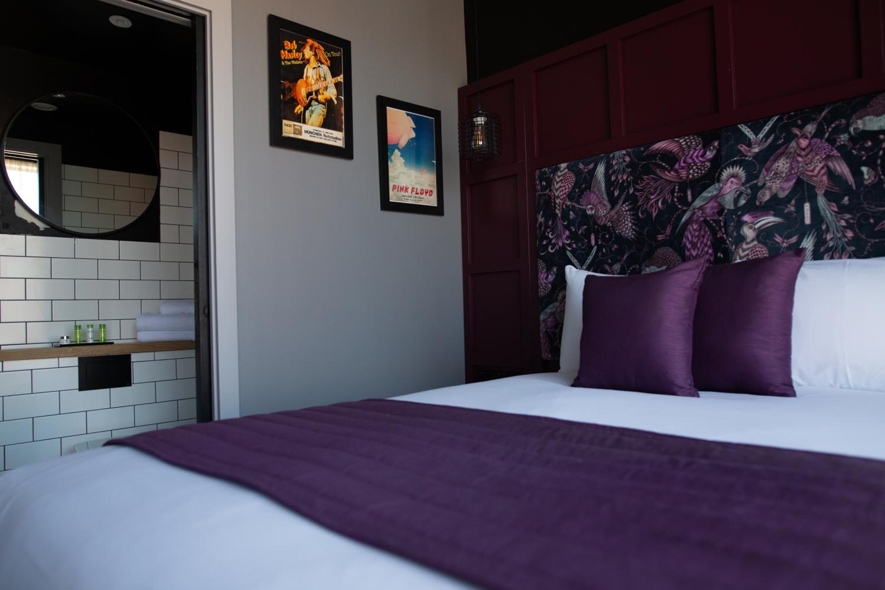 Una habitación de hotel con cama, espejo, estante con artículos de aseo personal y dos carteles en la pared.
