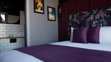 Una habitación de hotel con cama, espejo, estante con artículos de aseo personal y dos carteles en la pared.