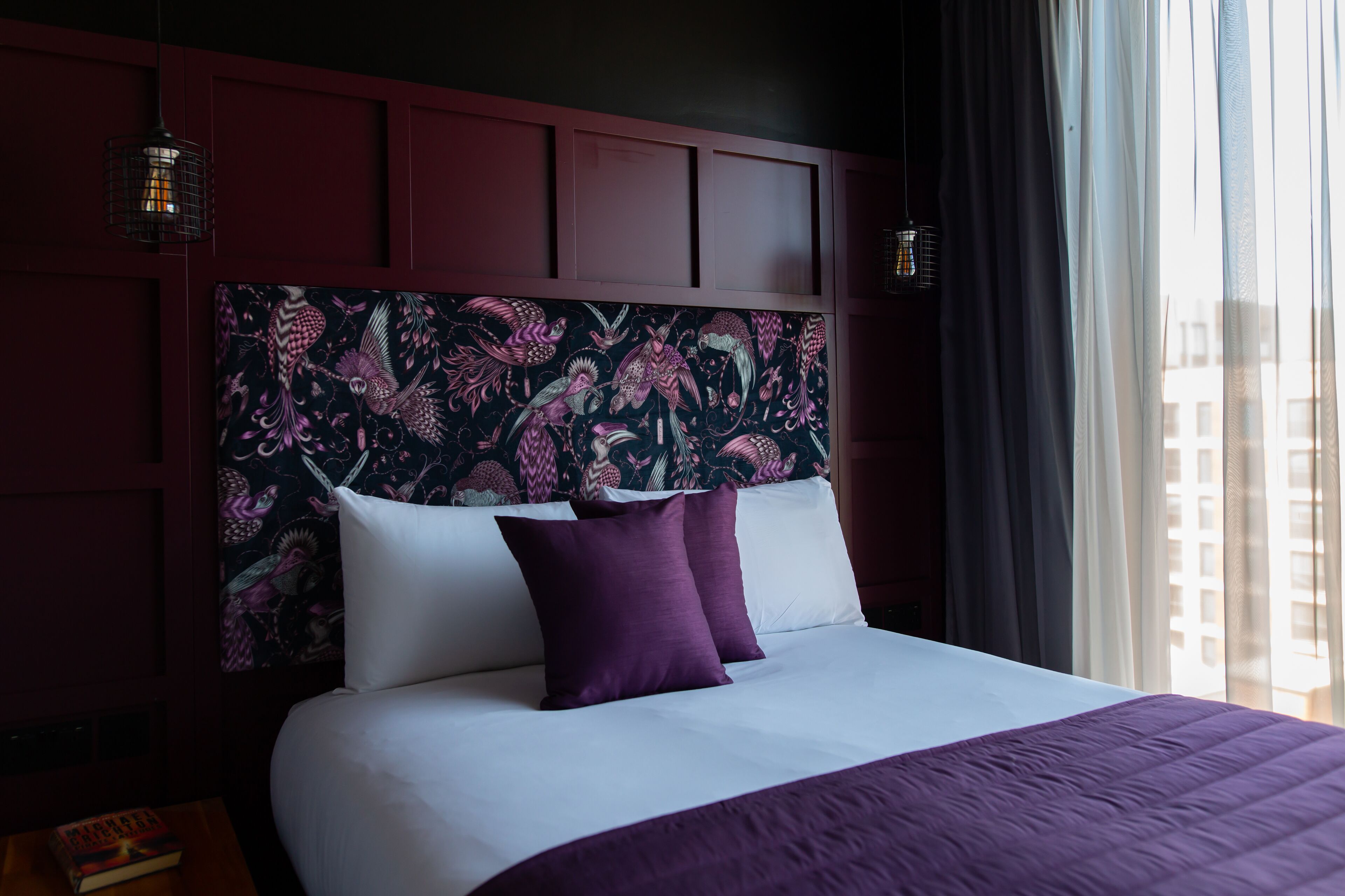 A hotel room with a large bed, dark wood paneling, and a floral-patterned headboard.