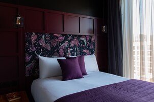 Una habitación de hotel con una cama grande, paneles de madera oscura y un cabecero estampado con motivos florales.