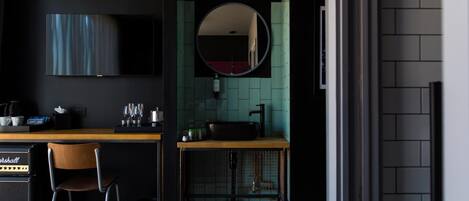 Una camera d'albergo moderna con un letto, una scrivania con una sedia, una televisione, un lavandino e uno specchio.