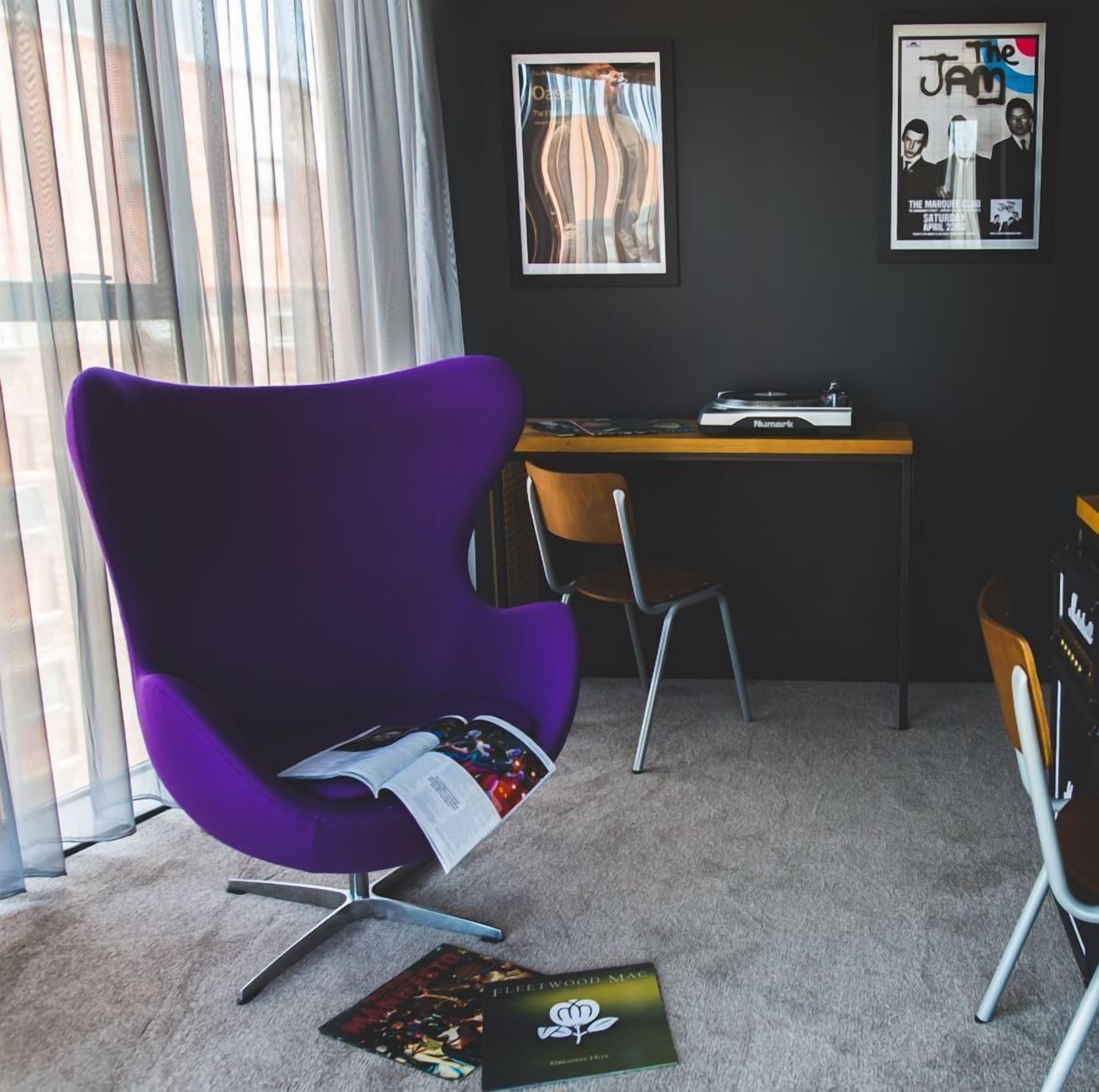 A modern office space with a purple chair, a desk with a turntable, and a poster on the wall.