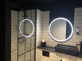 Un bagno moderno con due specchi illuminati, una cabina doccia in vetro e un lavandino nero.