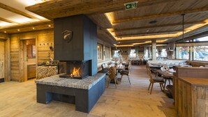 A spacious indoor area with a stone fireplace, wooden ceiling beams, and a dining area with tables and chairs.