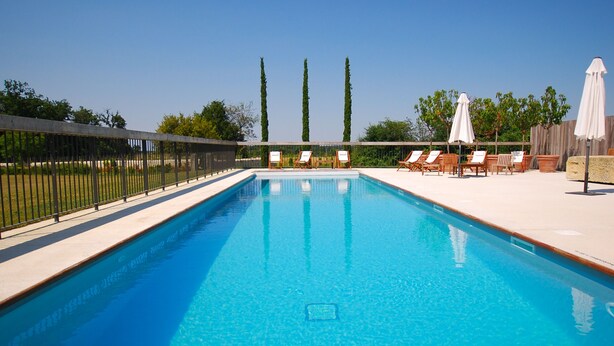 A rectangular swimming pool with clear blue water, surrounded by a white tiled deck. There are lounge chairs and umbrellas on the right side. - Les Gîtes de l'Ermitage (Terce)