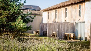 A rustic building with a wooden exterior, a tiled roof, and a fenced garden area with seating. - Les Gîtes de l'Ermitage (Terce)