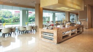 Un hall d’hôtel moderne avec un comptoir d’accueil en marbre, des murs en verre et une vue sur la verdure environnante.
