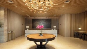 Un hall d’entrée moderne avec une table ronde en bois, une grande peinture abstraite et un comptoir d’accueil.