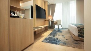 Une chambre d’hôtel moderne avec une armoire en bois, un téléviseur à écran plat, un bureau avec une lampe, un lit recouvert d’une courtepointe à motifs et une grande fenêtre avec des rideaux.