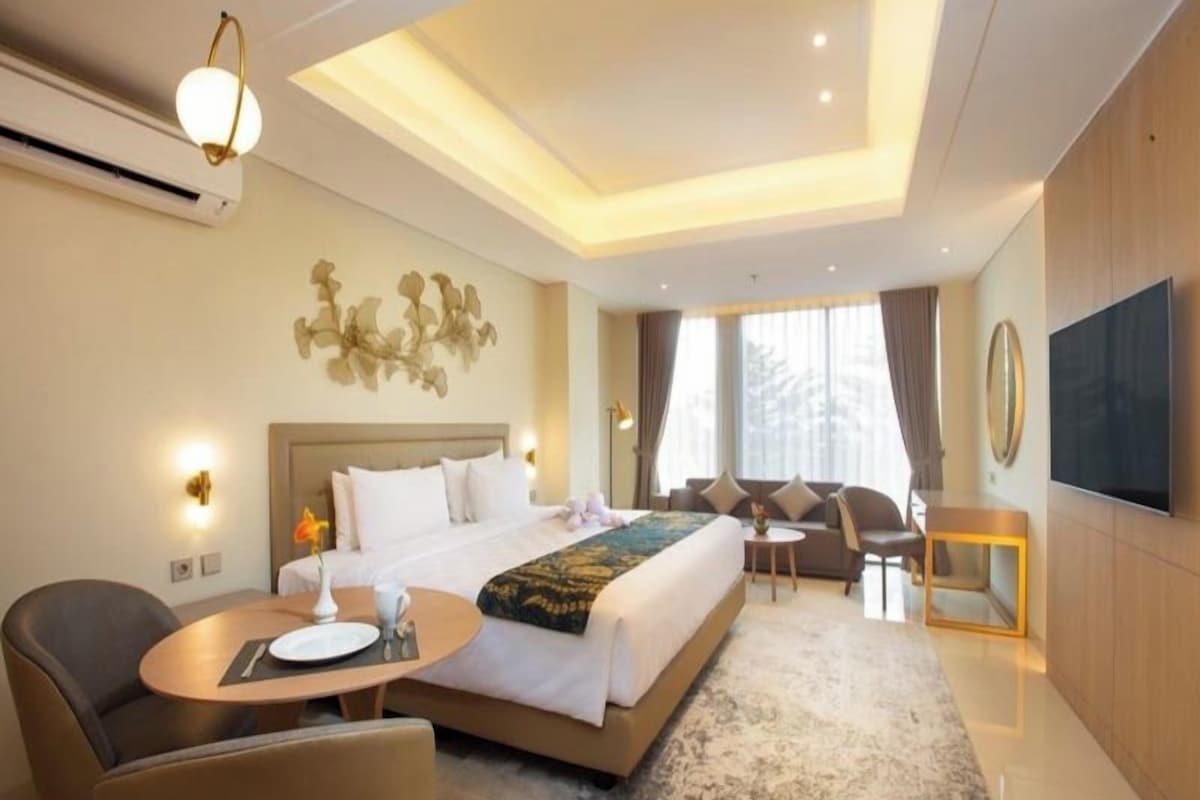 A modern hotel room with a large bed, a seating area, a flat-screen TV, and a wall-mounted artwork.