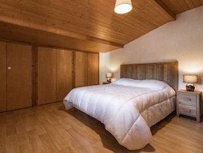 Une chambre avec un plafond en bois, un grand lit, des armoires en bois et deux lampes de chevet.
