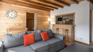 Ein modernes Wohnzimmer mit Holzboden, einem grauen Sofa mit roten Kissen, einer Holzbar und einer Küchenzeile inklusive Mikrowelle.