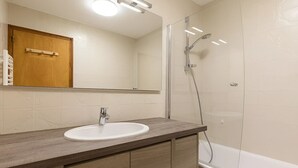 Ein Badezimmer mit einem Holzkosmetikschrank, einem weißen Waschbecken, einem Spiegel und einer Duschkabine.