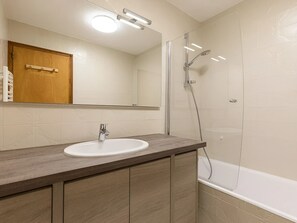 A bathroom with a wooden vanity, a white sink, a mirror, and a glass-enclosed shower.