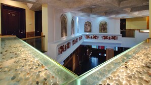 A hotel lobby with a glass-bottomed staircase, ornate ceiling, and a reception desk. - Hotel Pratap Heritage (Mahabaleshwar)