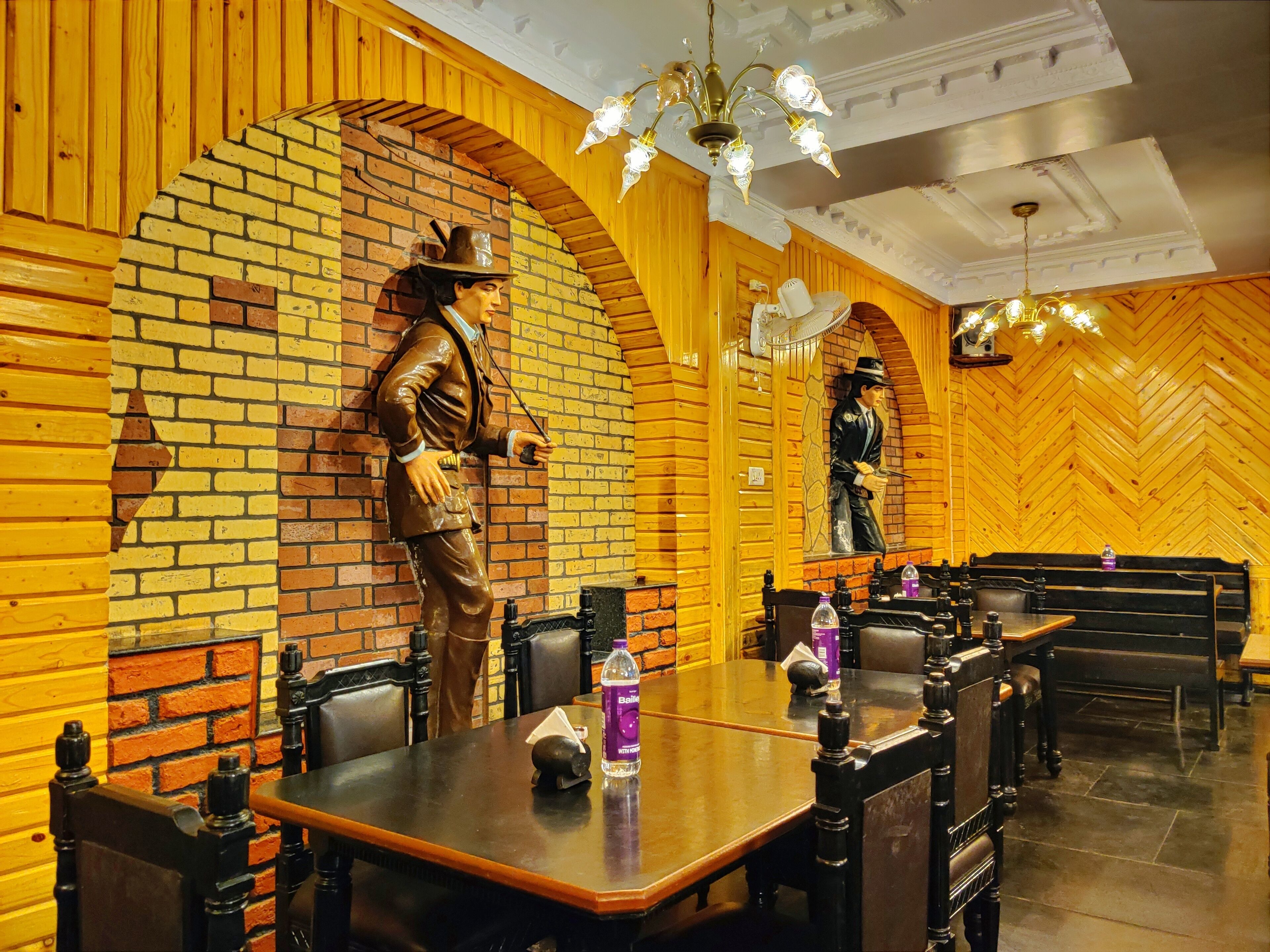 A restaurant with brick walls, wooden paneling, and a chandelier. There are tables and chairs, and a statue of a man holding a sword.