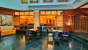 A spacious lobby with a high ceiling, a central seating area with tables and chairs, and a bar area with a large mirror and decorative elements. - Hotel Pratap Heritage (Mahabaleshwar)