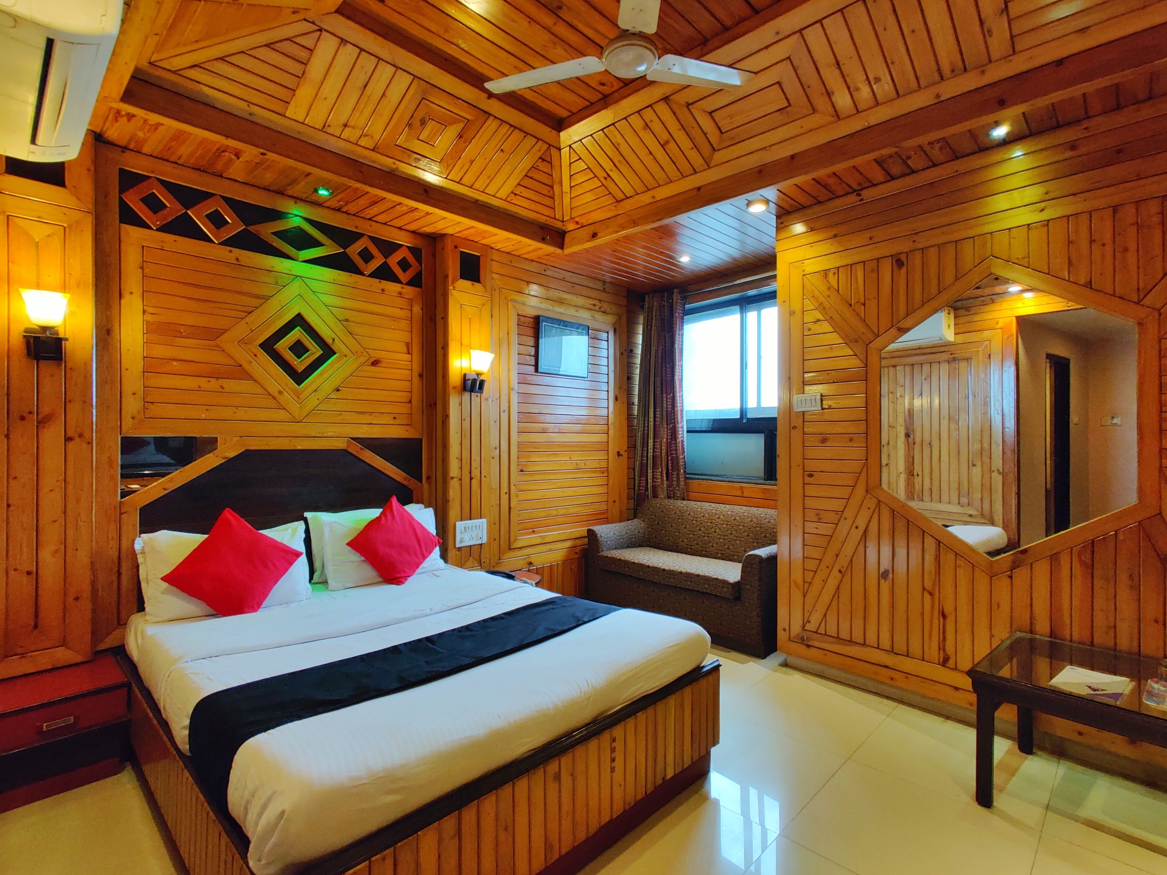 A wooden cabin room with a bed, a sofa, a mirror, and a ceiling fan.