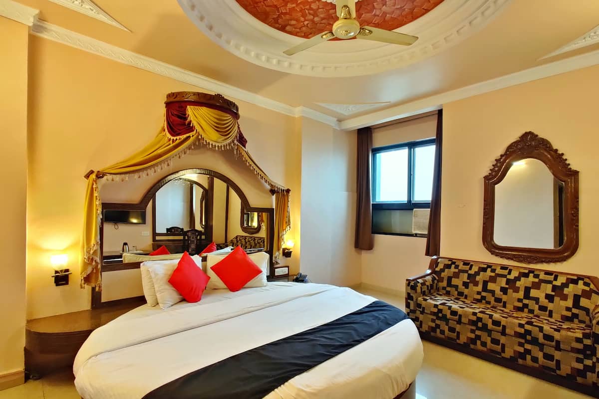 Una habitación de hotel con una cama grande, dosel, sofá, ventilador de techo, espejo grande y ventana.
