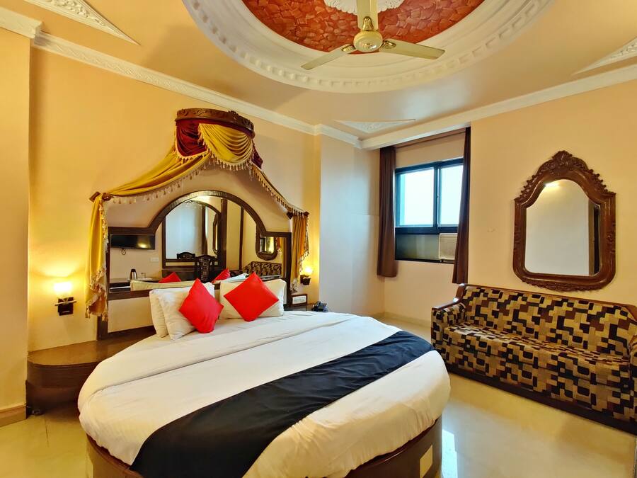 A hotel room with a large bed, a canopy bed, a sofa, a ceiling fan, a large mirror, and a window.